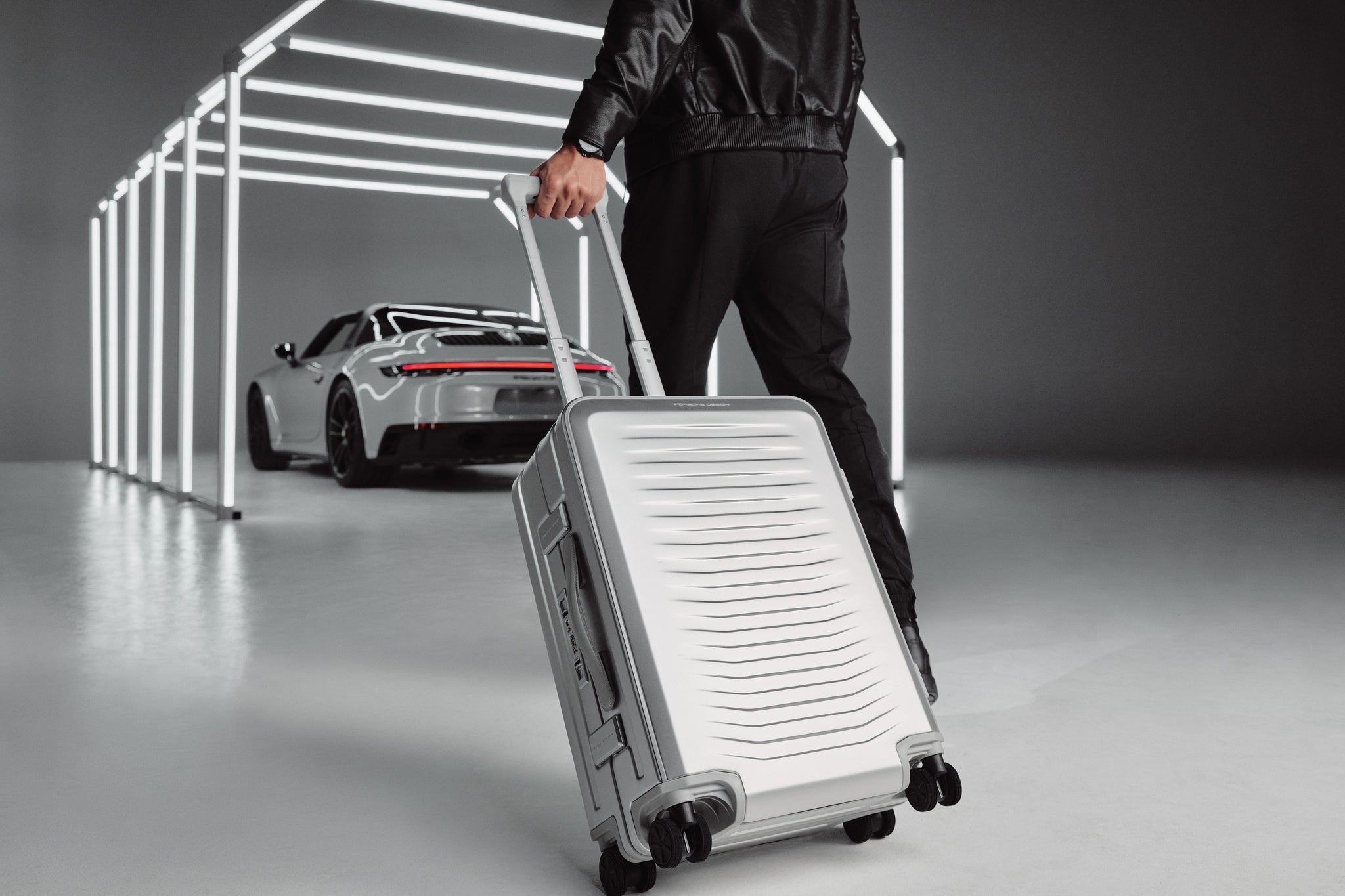 Person pulling a silver suitcase with a car in the background